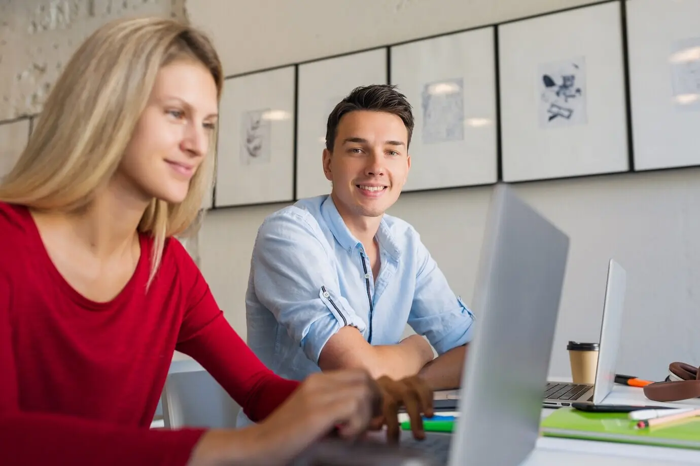 Online-Remote-Arbeitende: ein junger Mann und eine junge Frau, die am Laptop in einem Open-Space-Coworking-Büroraum arbeiten.